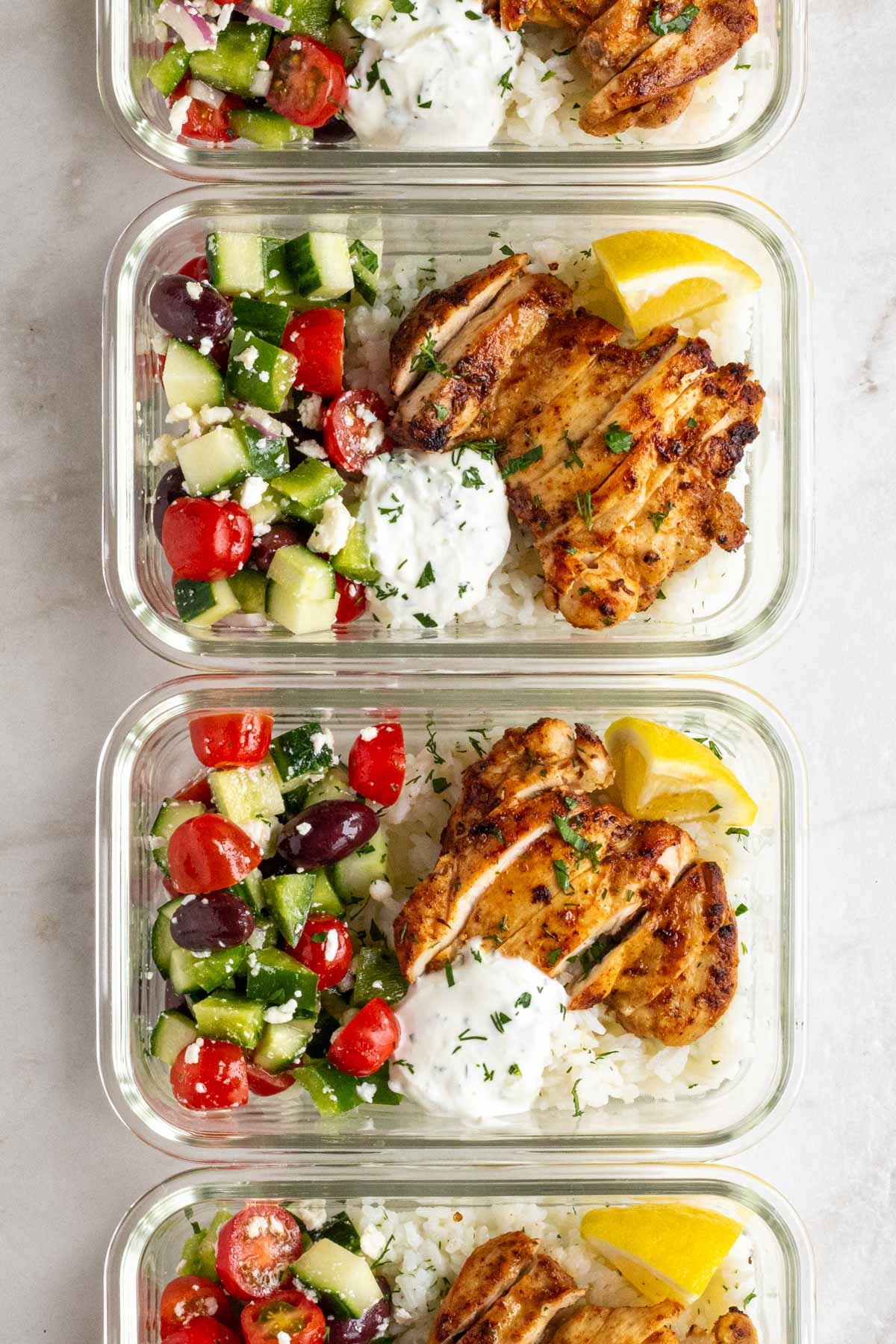 A vertical line up of Greek chicken meal prep bowls in glass containers.