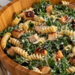 Close up kale chicken caesar pasta salad in a large wooden bowl.