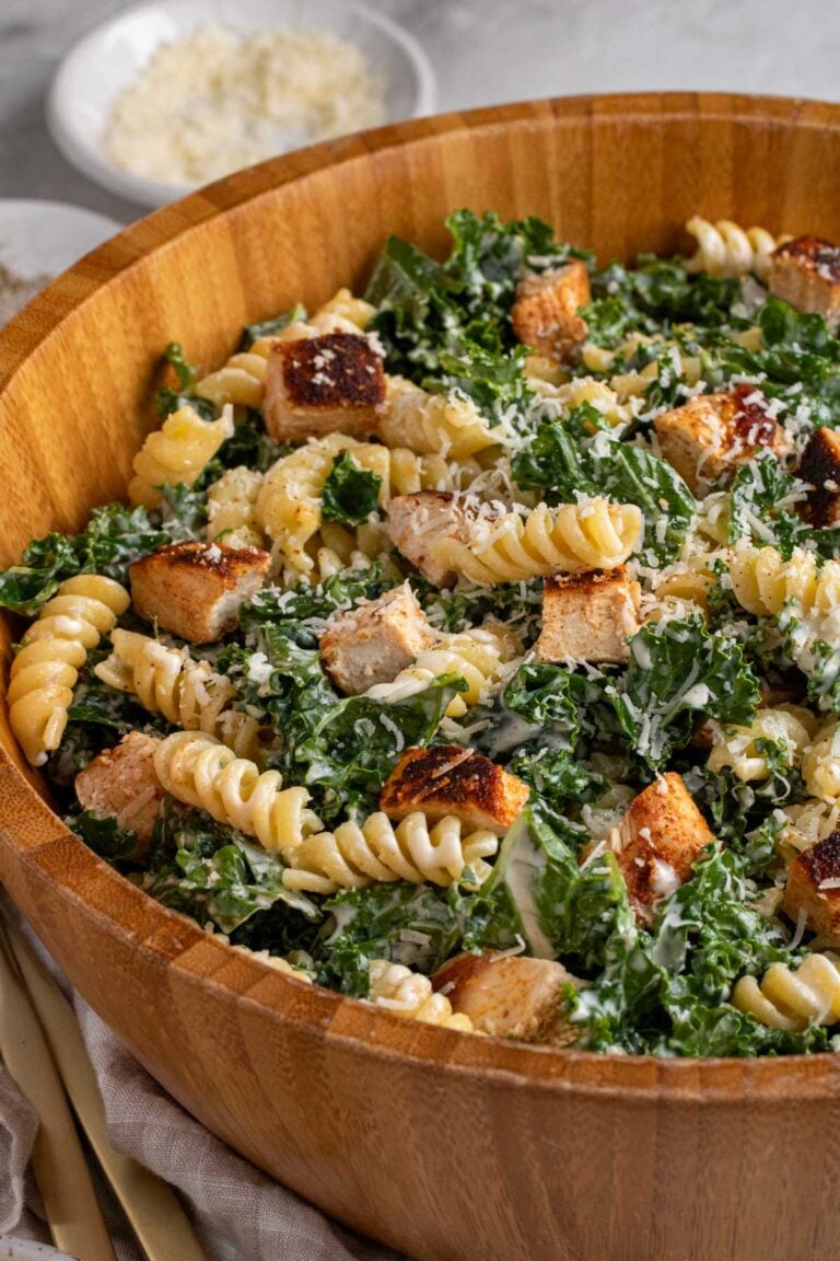 Close up kale chicken caesar pasta salad in a large wooden bowl.