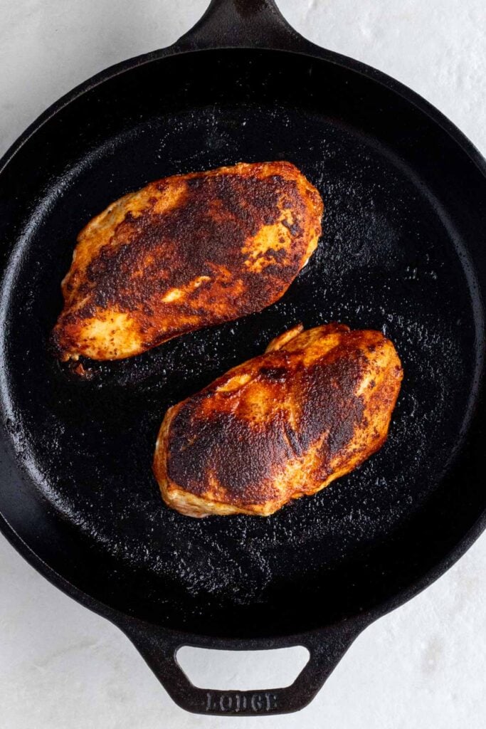 Cast-iron skillet with two grilled chicken breasts.