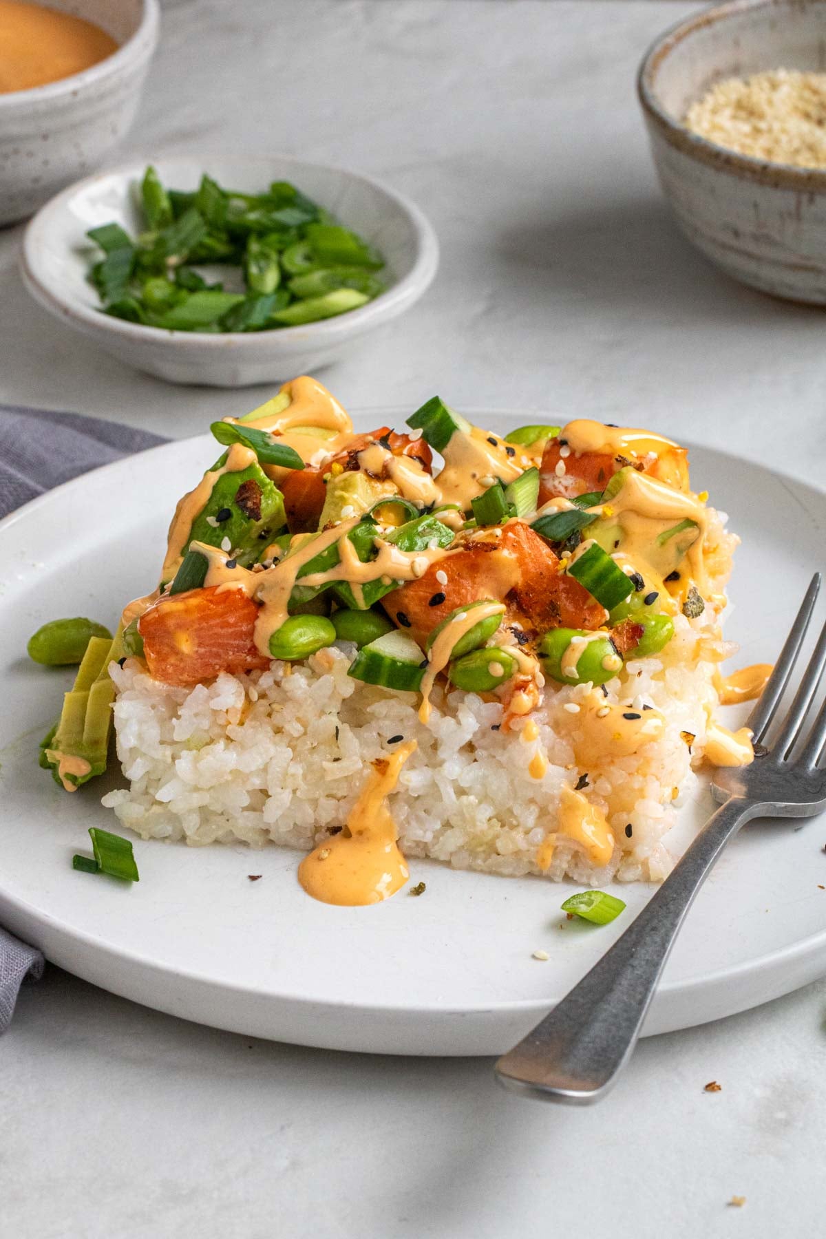 Slice of sushi salmon bake on a white plate with spicy mayo drizzle on top with a fork on the side.