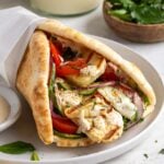 Mediterranean grilled halloumi wrap with tomatoes, cucumber, red onion, fresh herbs, and garlic sauce on a white plate on a white background.