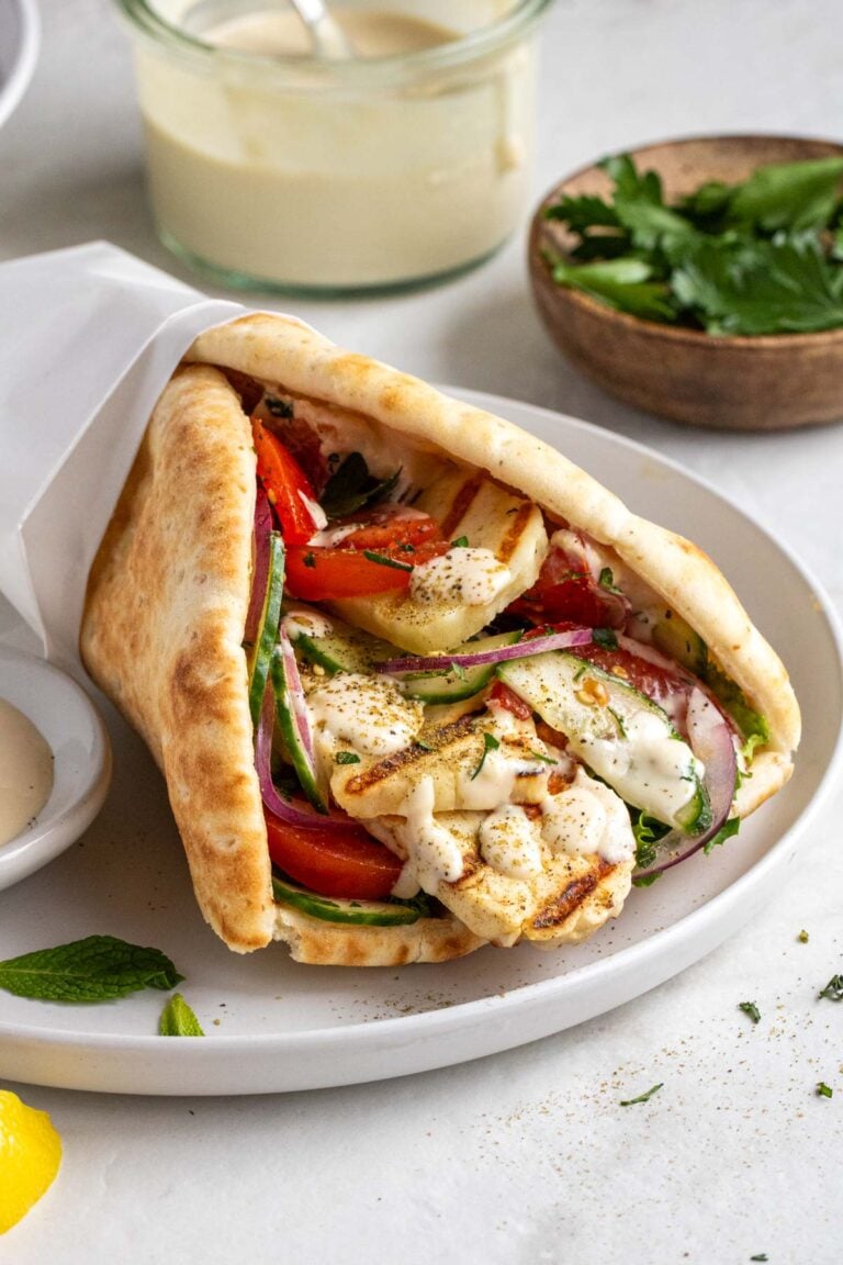 Mediterranean grilled halloumi wrap with tomatoes, cucumber, red onion, fresh herbs, and garlic sauce on a white plate on a white background.