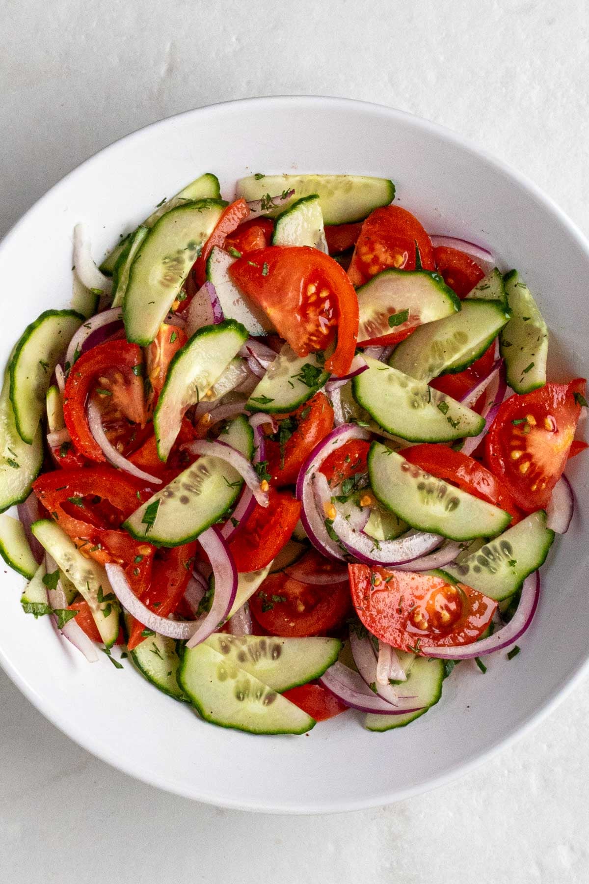 White bowl of cucumber tomato salad on a white background.