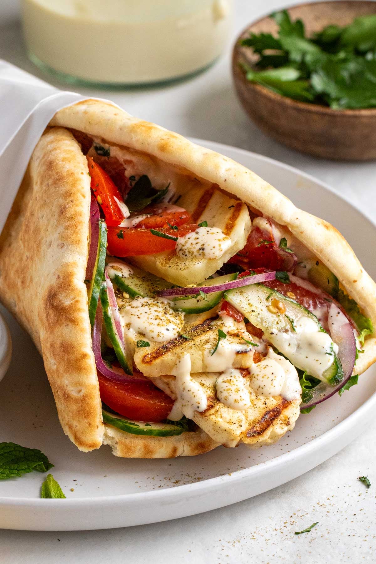 Close up of a Greek-inspired grilled halloumi wrap on a white plate.