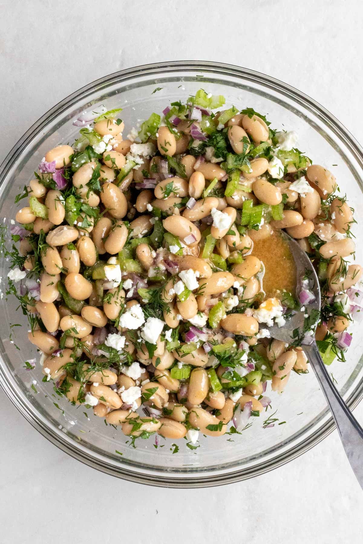 Glass bowl of white bean and vegetable mixture with feta cheese and dressing on top.
