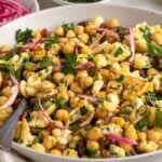 Close of up a beige speckled bowl filled with roasted cauliflower salad with a serving spoon.