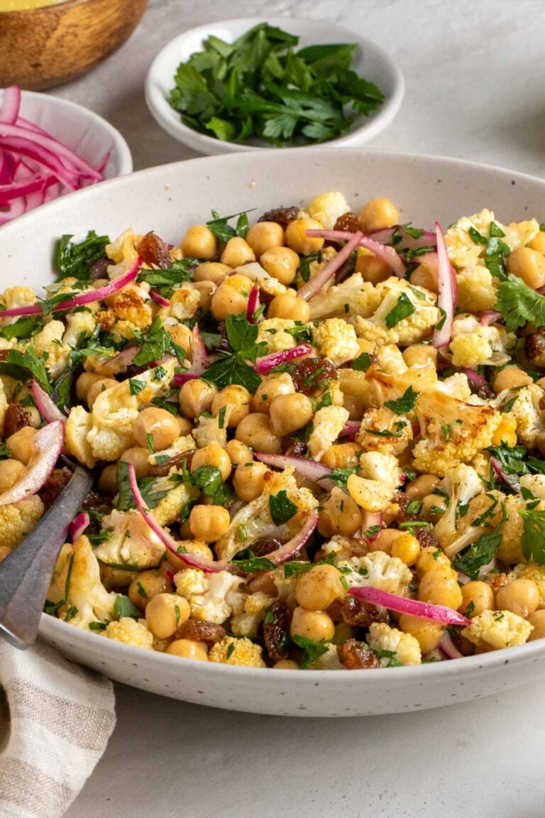 Close of up a beige speckled bowl filled with roasted cauliflower salad with a serving spoon.