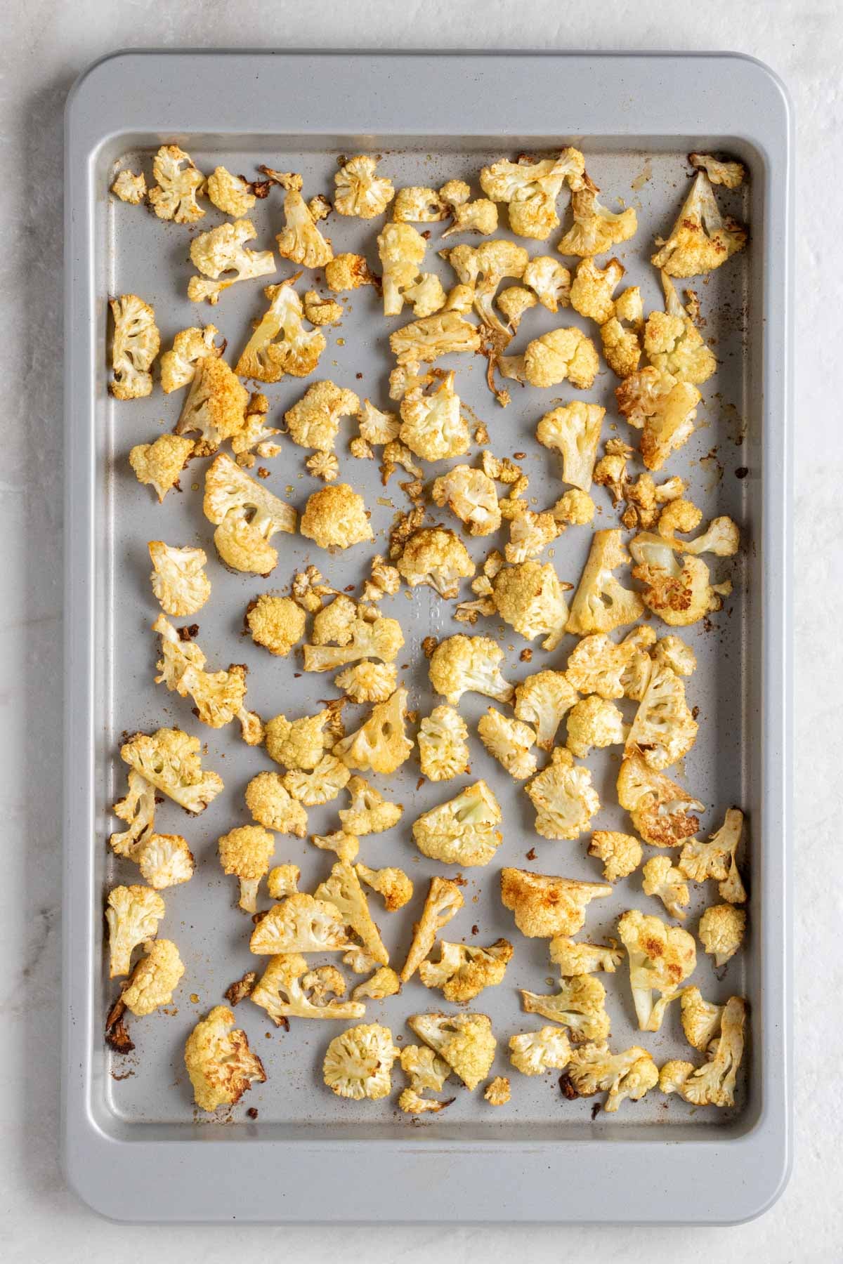 Baking sheet with roasted cauliflower florets on a white background.