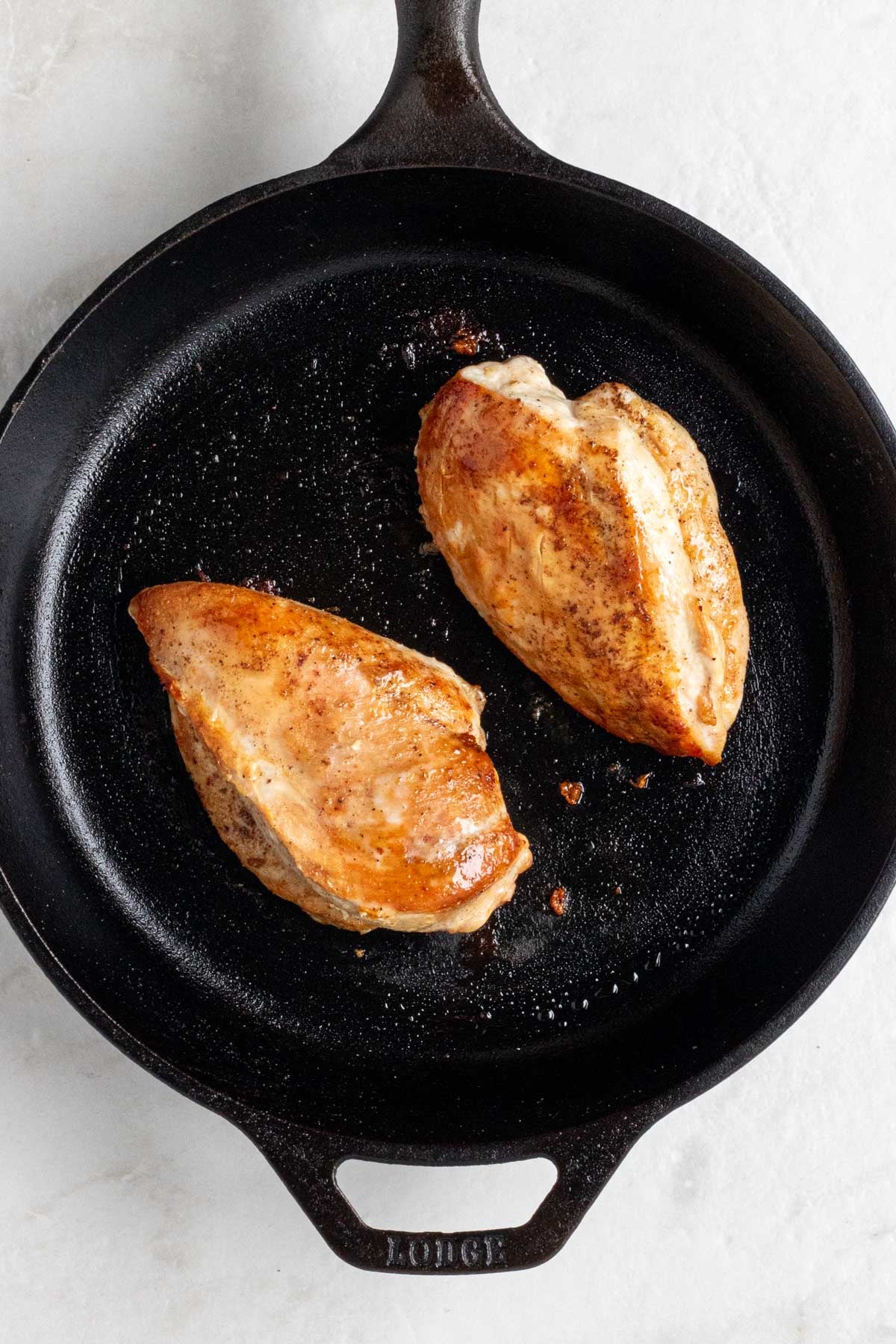 Cast-iron skillet with two cooked chicken breasts.