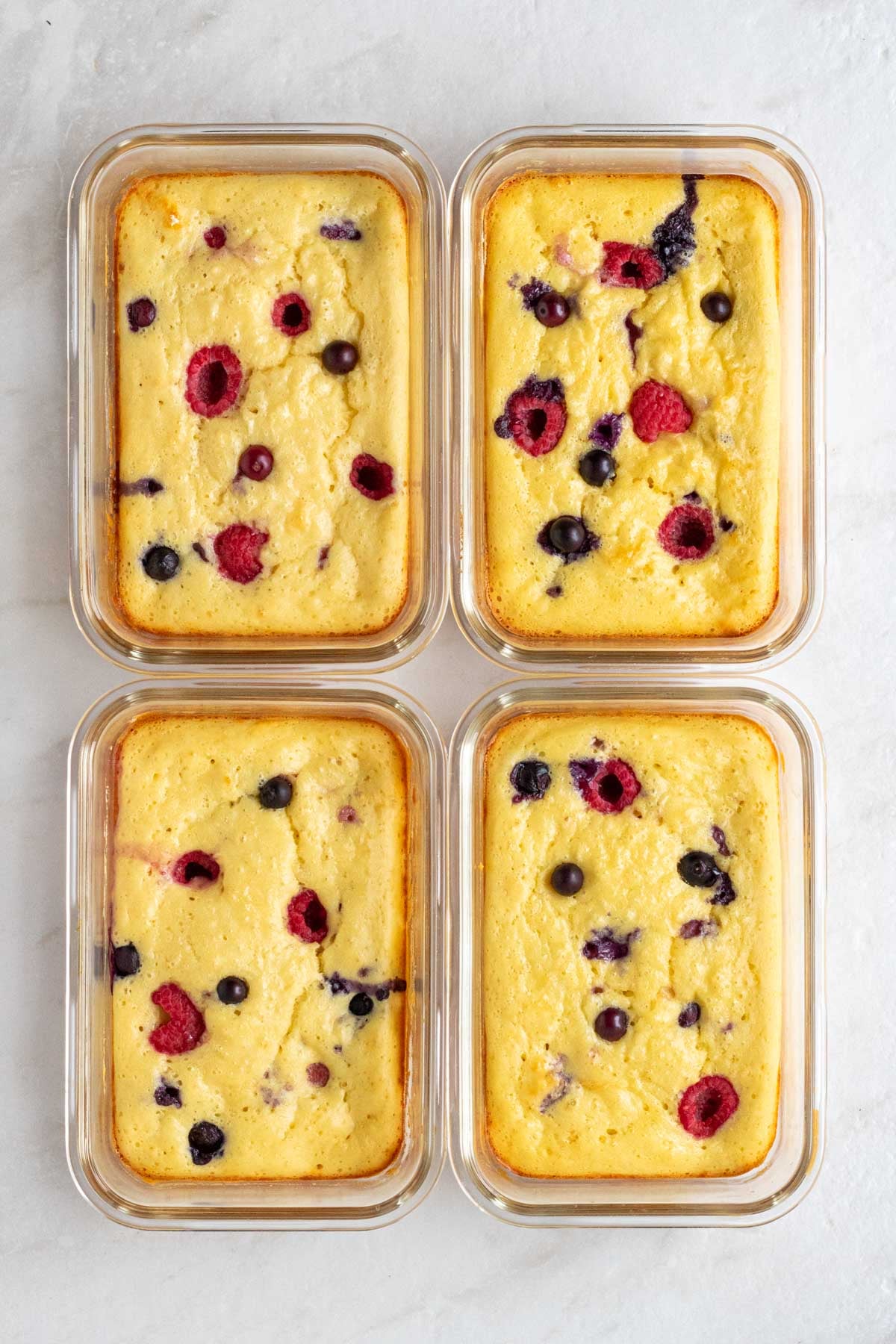 Four protein pancake bowls in glass meal prep containers on a white background.