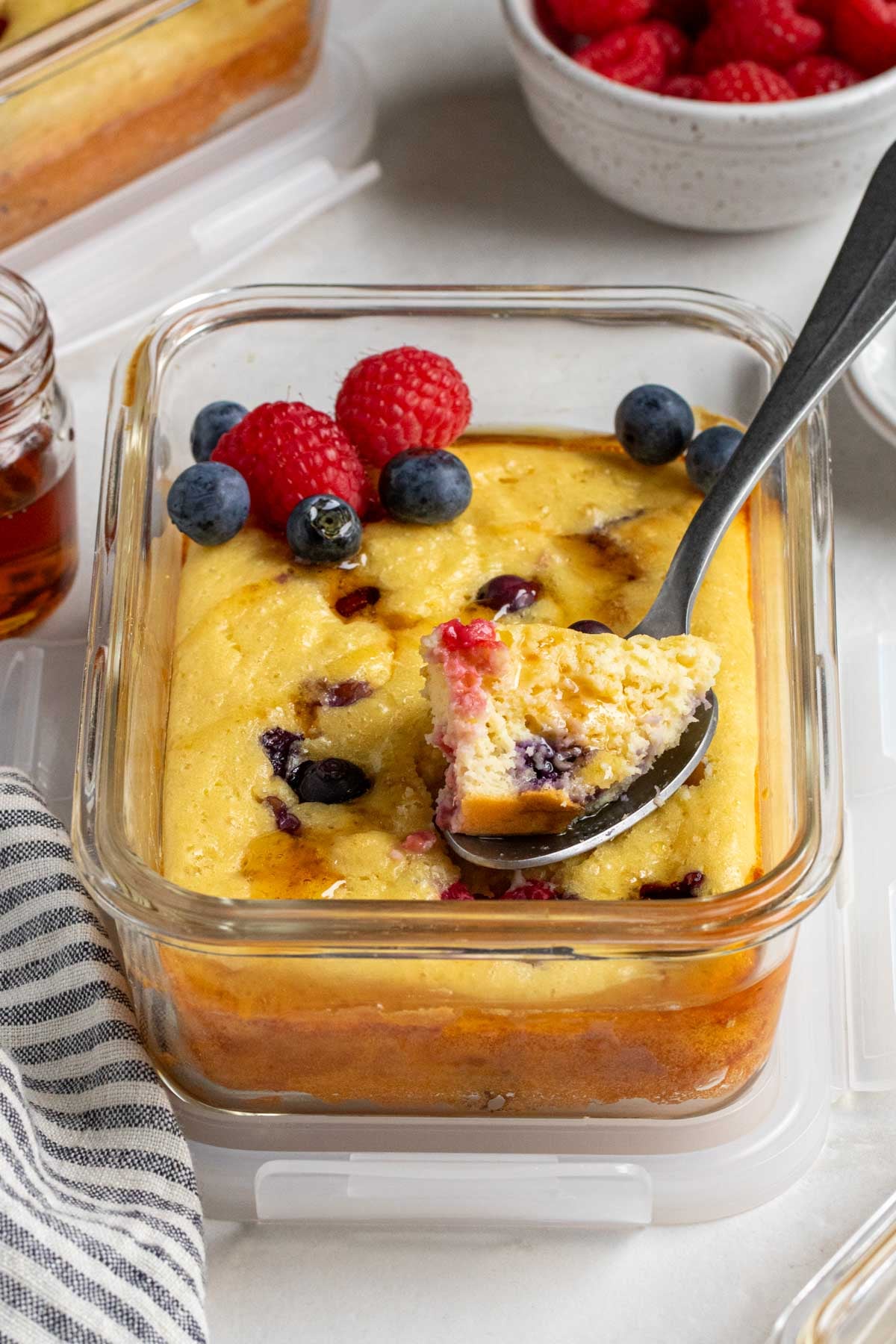 Close up of a protein pancake meal prep bowl with maple syrup on top with a spoonful on a spoon.