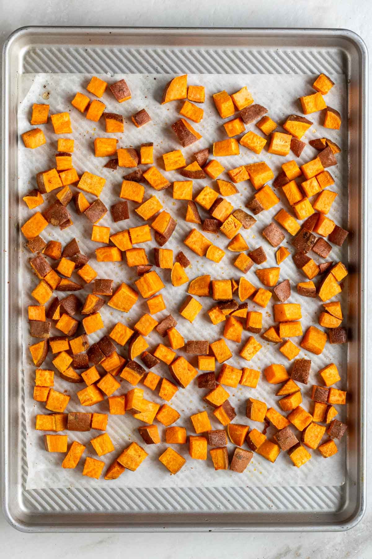 Large sheet pan with parchment paper with diced roasted sweet potatoes on top.