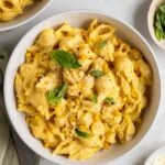 Two bowls creamy corn pasta with fresh basil on top on a light green tea towel with a fork on the side and small bowls of red pepper flakes and freshly grated parmesan cheese on the side.