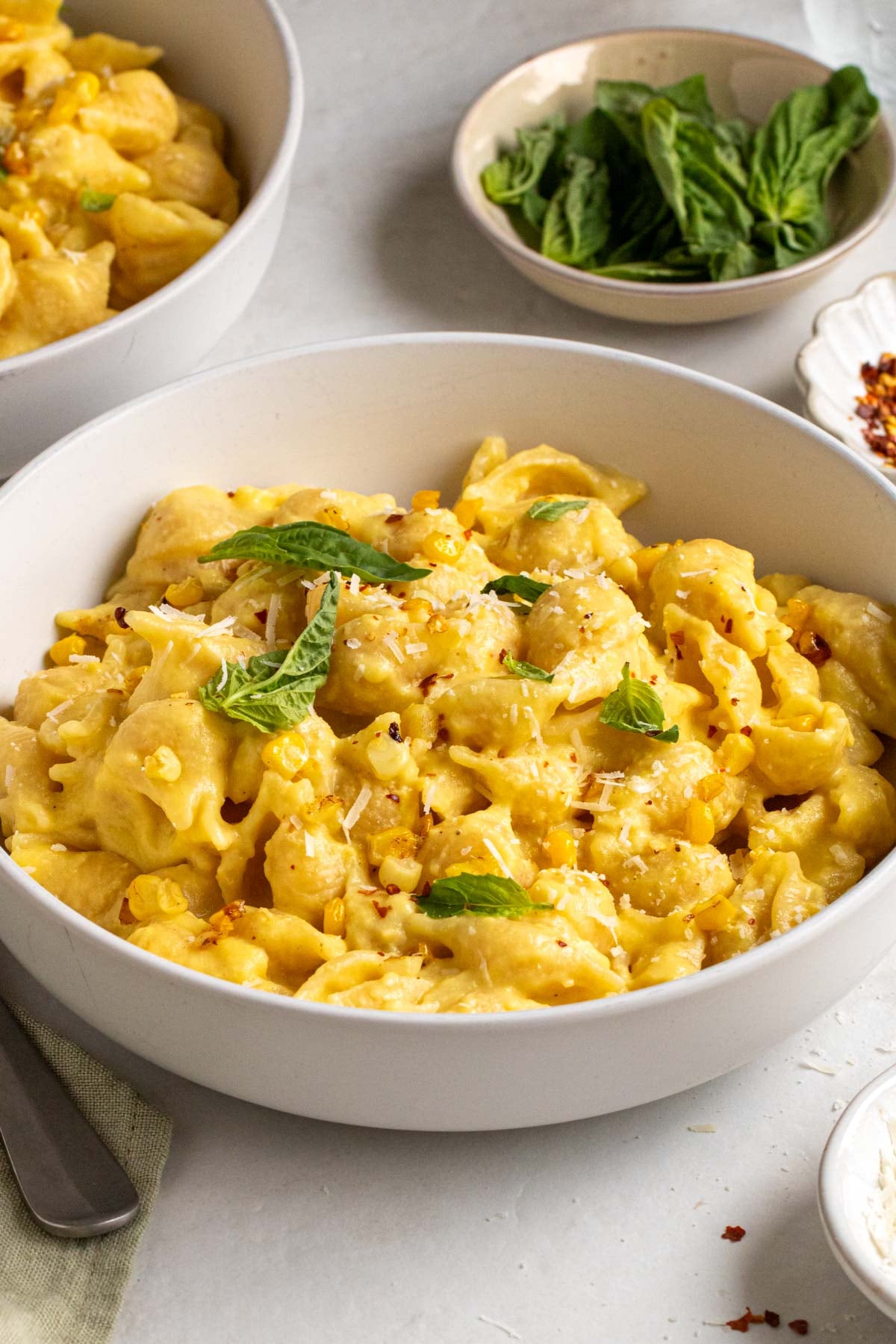 Close up of a bowl of shell pasta with creamy corn sauce with a bowl of fresh basil in the background.