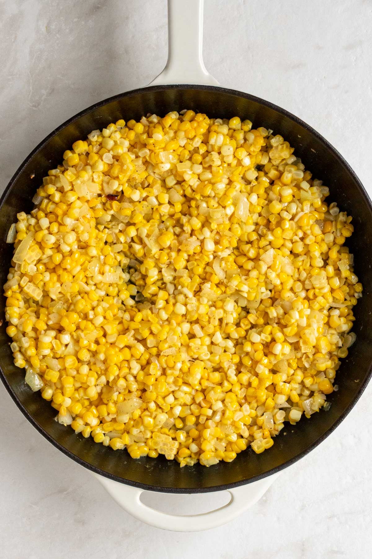 Large cast-iron pan with sautéed onion, garlic, and corn kernels.