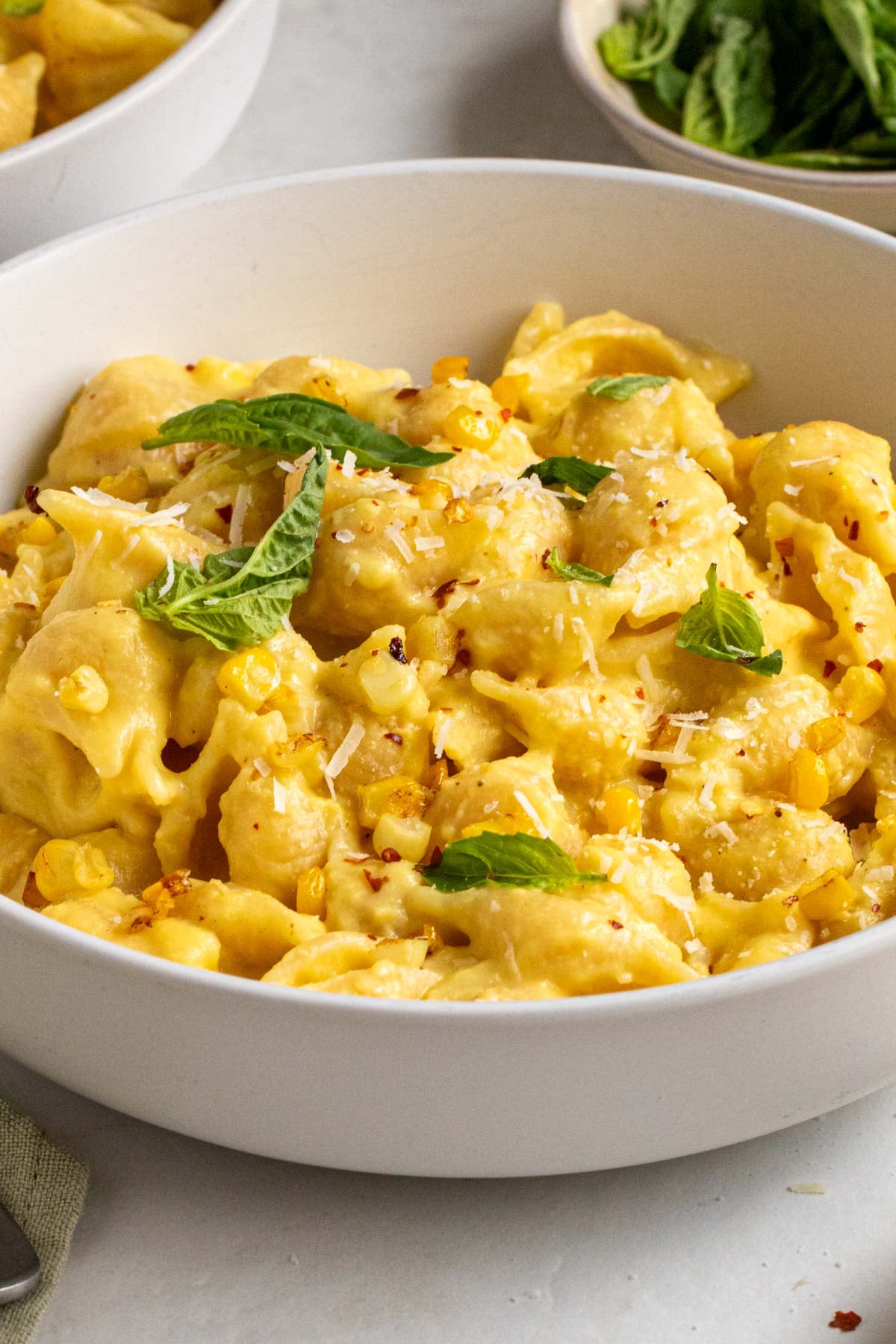 Close up of creamy corn pasta in a bowl with freshly grated parmesan cheese, basil, and red pepper flakes on top.