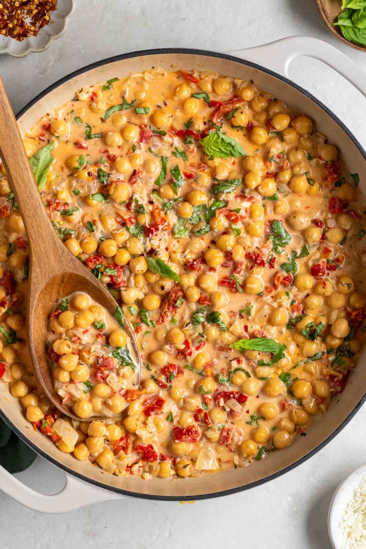 Large pot of Marry me chickpeas with fresh basil on top with a wood serving spoon.
