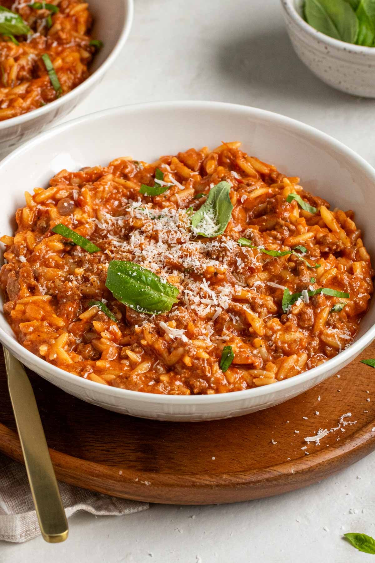 Close of up of a bowl of ground beef orzo pasta with basil and parmesan cheese on top.