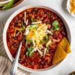 Two bowls of slow cooker turkey chili with sour cream, shredded cheese, fresh cilantro, and sliced green onion on top with tortilla chips on the side.