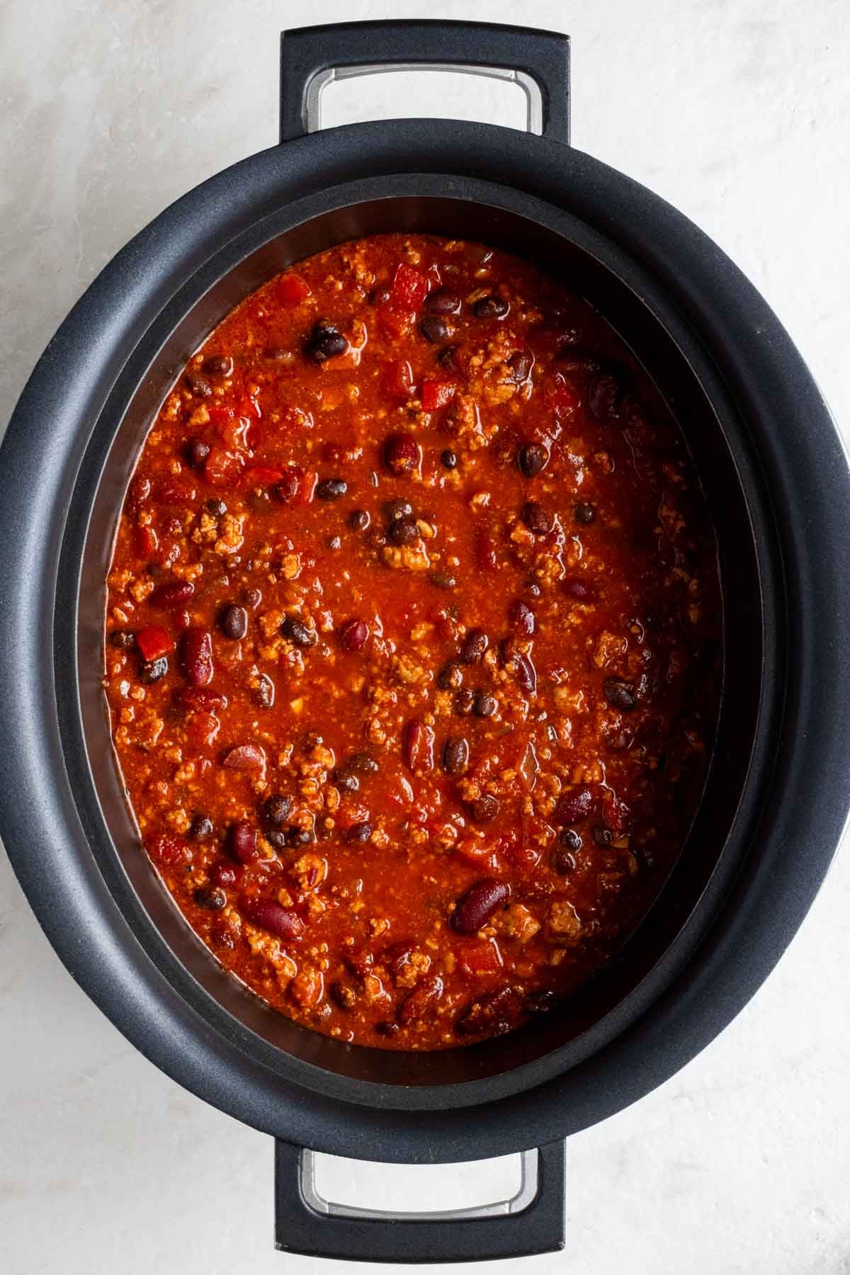 A large slow cooker of turkey chili on a white background.