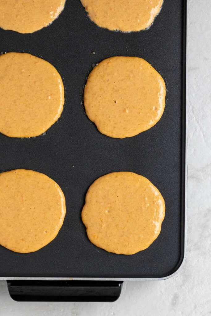 Raw sweet potato pancake batter cooking on an electric griddle.