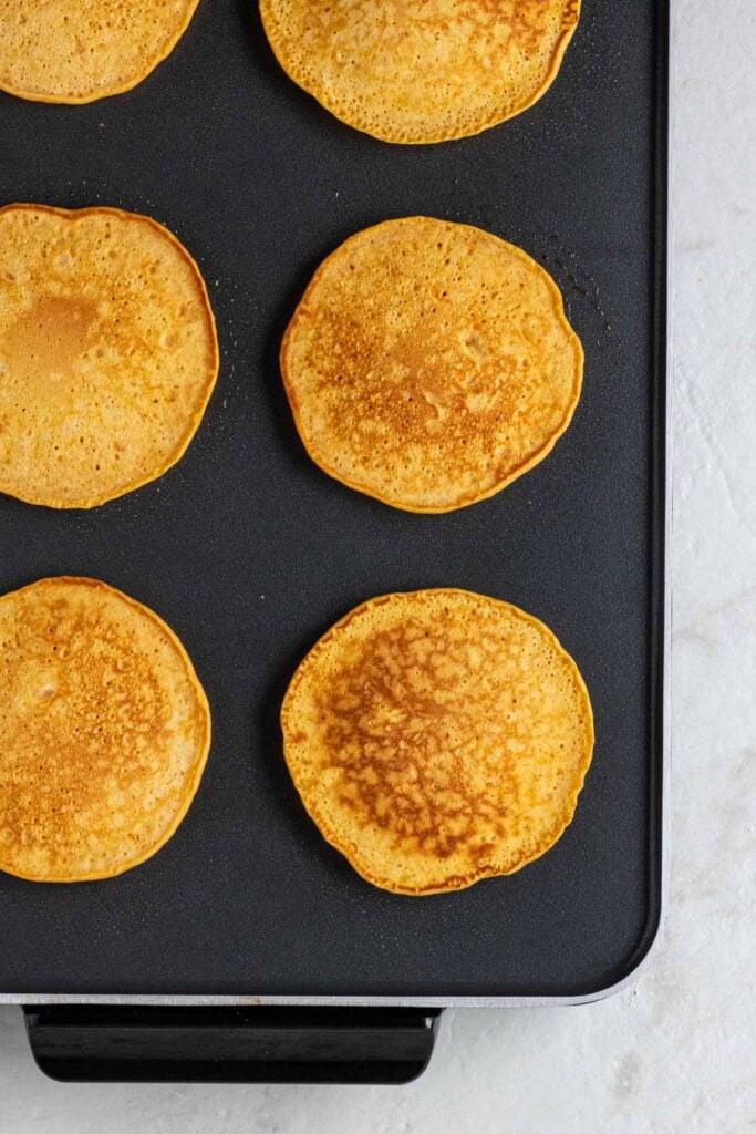 Sweet potato pancakes cooking on an electric griddle.