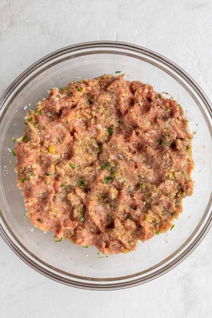 Glass bowl of chicken meatball mixture on a white background.